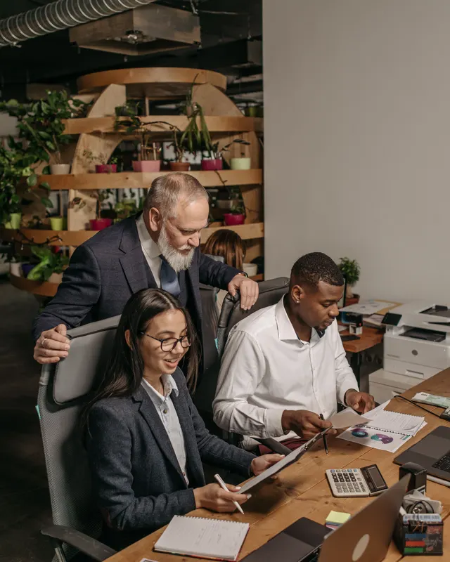 A manager reviewing work alongside two colleagues at a desk.